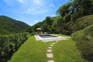 Ein rechteckiger Pool mit einem steinernen Pfad, umgeben von üppiger Vegetation und Hügeln.