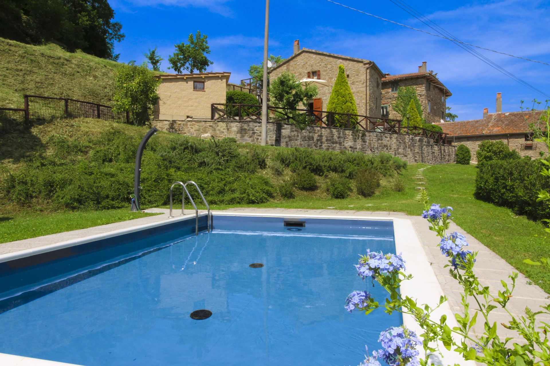 Una piscina con una parete in pietra e una casa sullo sfondo.