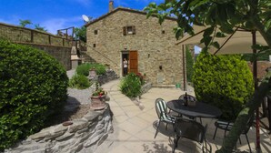Edificio de piedra con puerta de madera, una escalera y un patio con mesa y sillas.