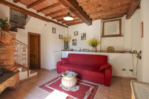 Ein gemütliches Wohnzimmer mit einem roten Sofa, einem Couchtisch und einem Kamin. Eine Treppe mit Holzwand und eine Tür zu einem anderen Raum sind ebenfalls zu sehen.