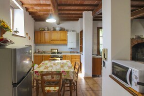 A kitchen with wooden cabinets, a refrigerator, a microwave, and a dining table with chairs.
