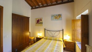Un dormitorio con una cama, dos mesitas de noche con lámparas, un armario de madera y un cuadro en la pared.