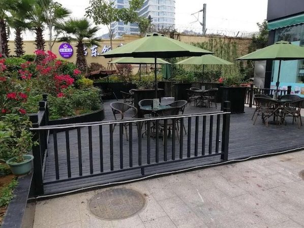 An outdoor patio area with tables and chairs, green umbrellas, and a wooden deck. - Xana Hotelle (Xiamen Railway Station) (Xiamen)