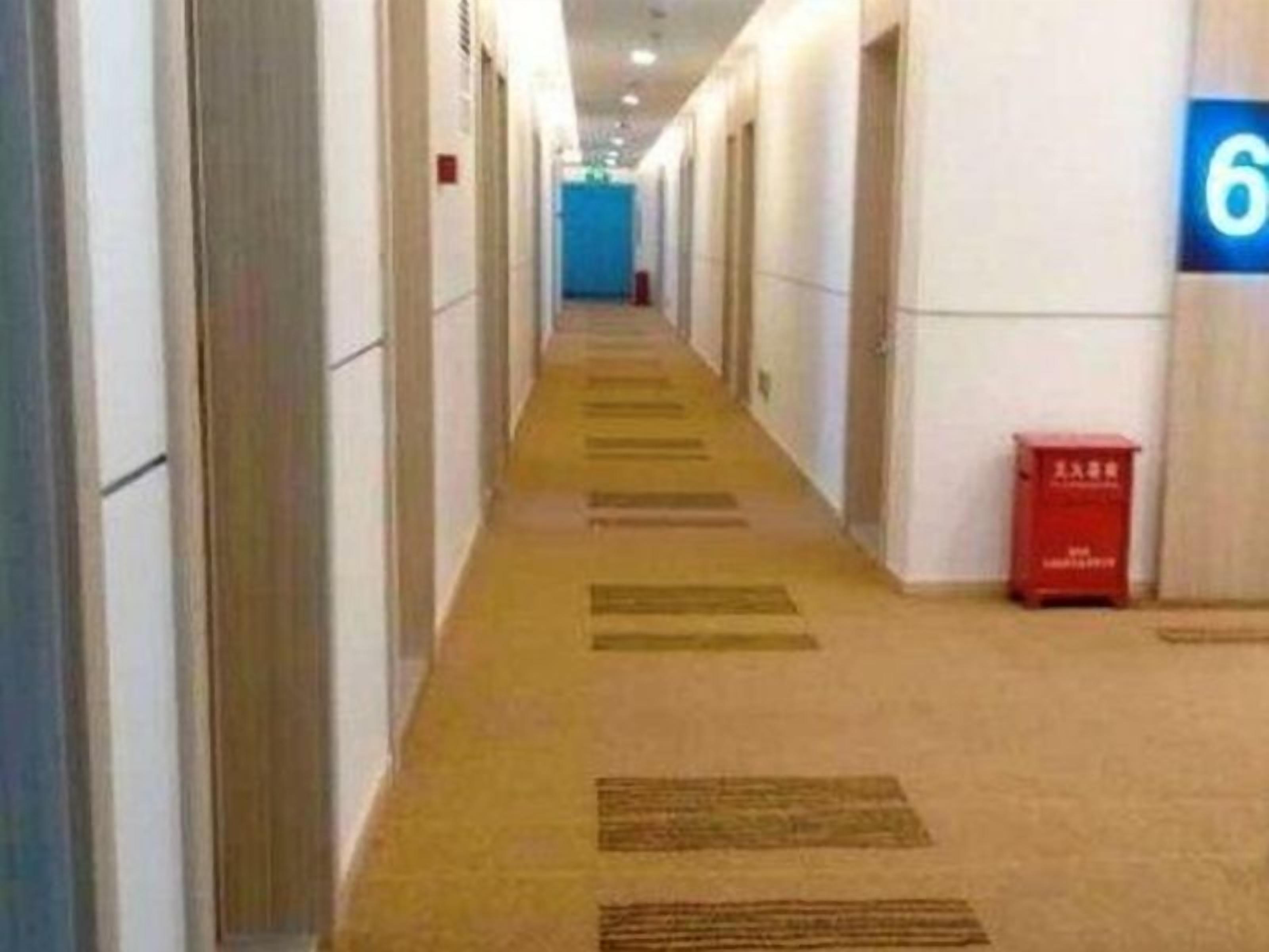 A hotel corridor with a carpeted floor, doors on both sides, and a red mailbox on the right.