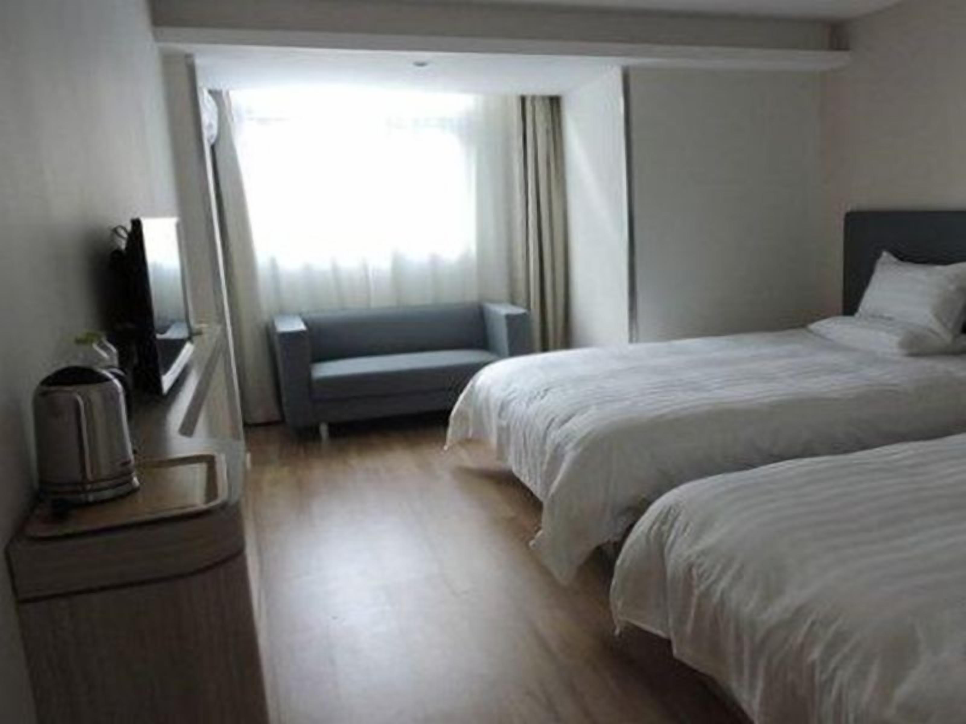 Une chambre d’hôtel avec deux lits, un petit coin salon, un bureau avec une lampe et une fenêtre avec des rideaux.