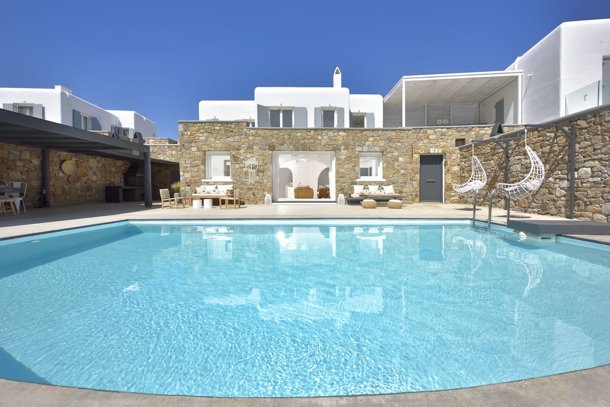 A swimming pool with stone walls, white buildings, and outdoor seating.