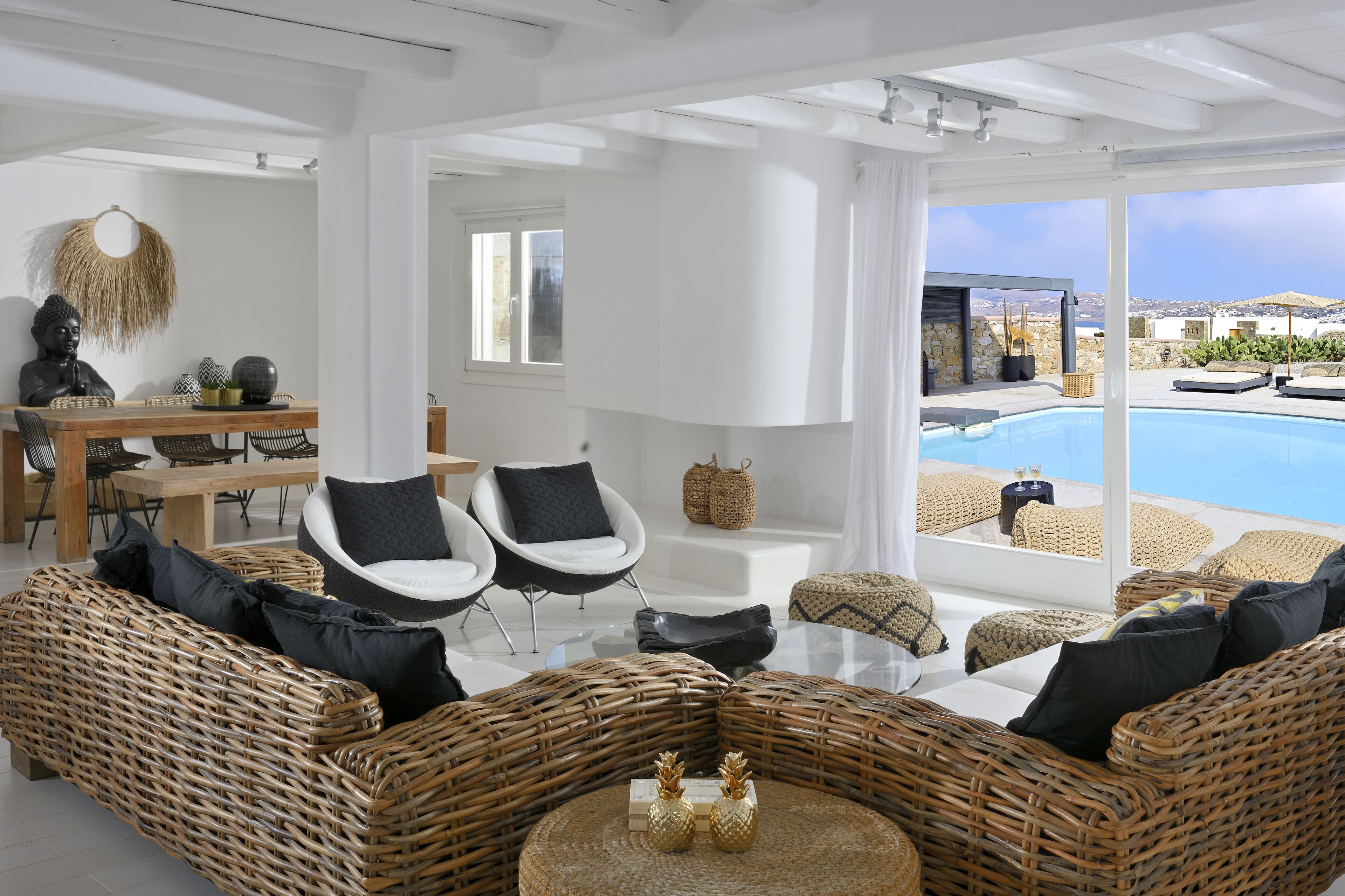 A modern, open-plan living area with a pool, wicker furniture, and a view of the sea.