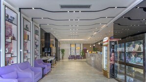 A hotel lobby with a reception desk, purple seating area, and a shop on the right. - Lavande Hotel (Wuhan)