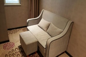 A corner sofa with a matching ottoman in a room with patterned carpet and a window with curtains. - Lavande Hotel (Wuhan)