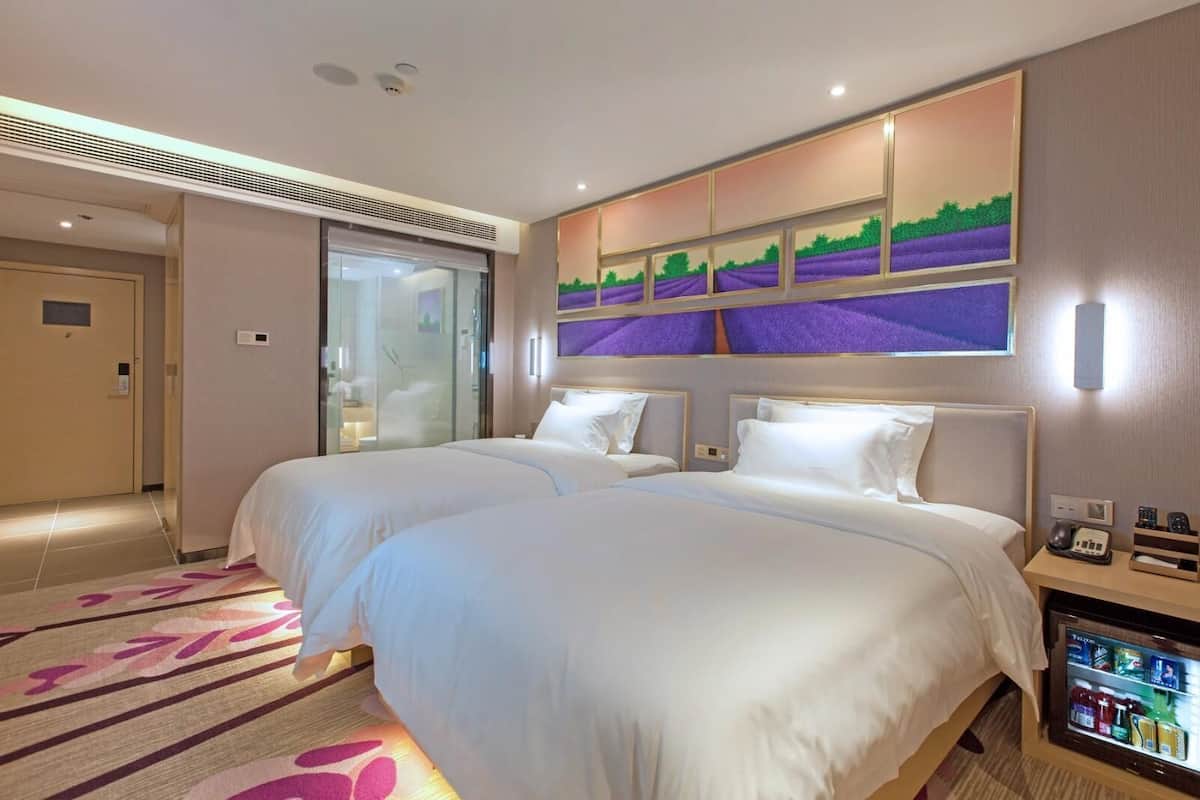 Habitación de hotel con dos camas, un minibar, cabina de ducha de vidrio y una obra de arte colgada en la pared.
