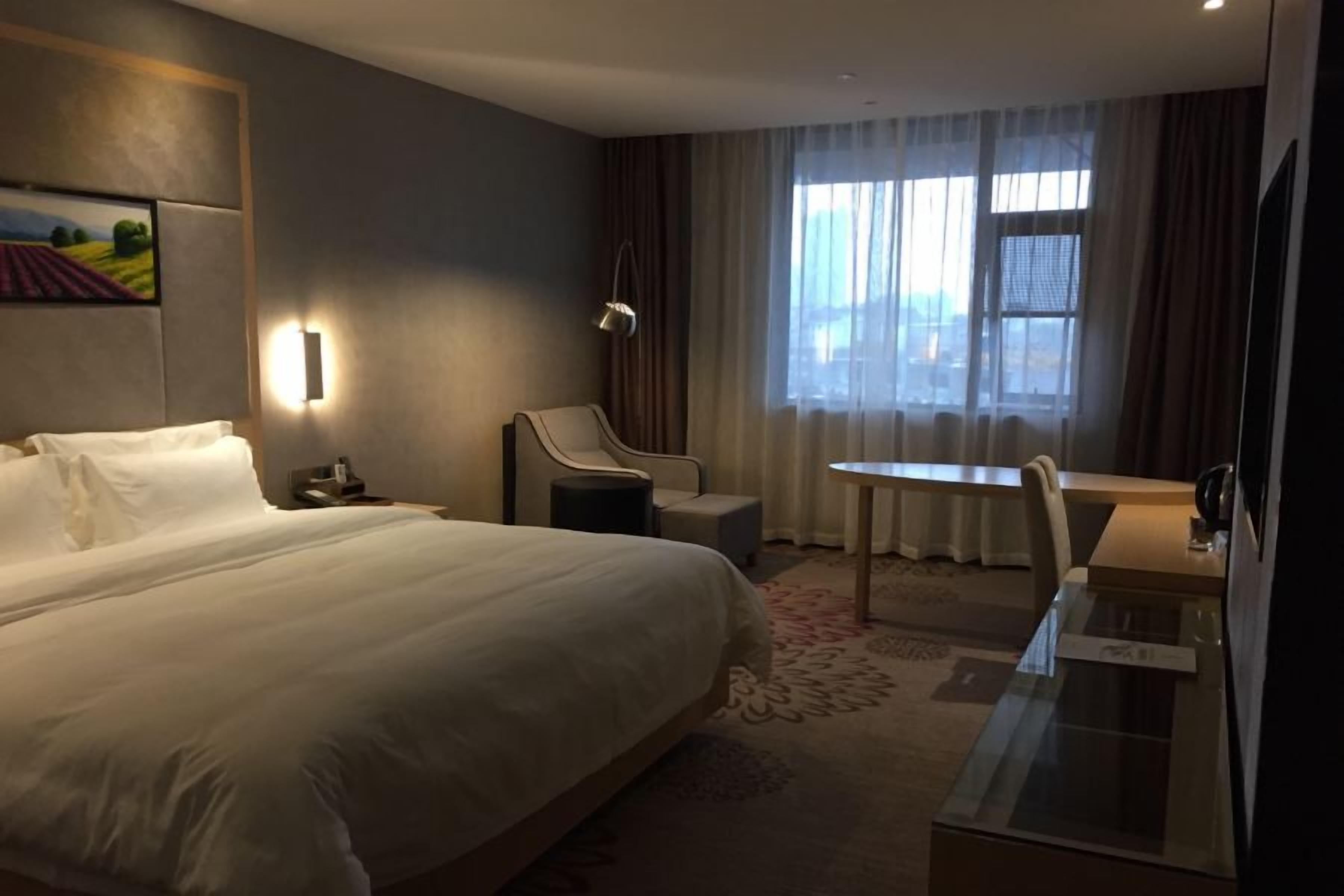 A hotel room with a large bed, a desk, a chair, and a window with curtains.