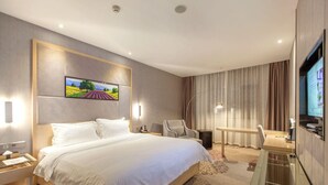 A hotel room with a large bed, a desk, a chair, a TV, and a painting on the wall. - Lavande Hotel (Wuhan)