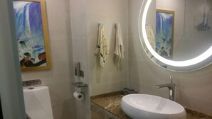 A bathroom with a white sink, a mirror with a circular light, a toilet, and a painting on the wall. - Lavande Hotel (Wuhan)