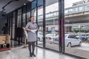 A hotel entrance with a glass facade, a receptionist, and a view of the street with cars and a bridge. - Lavande Hotel (Wuhan)