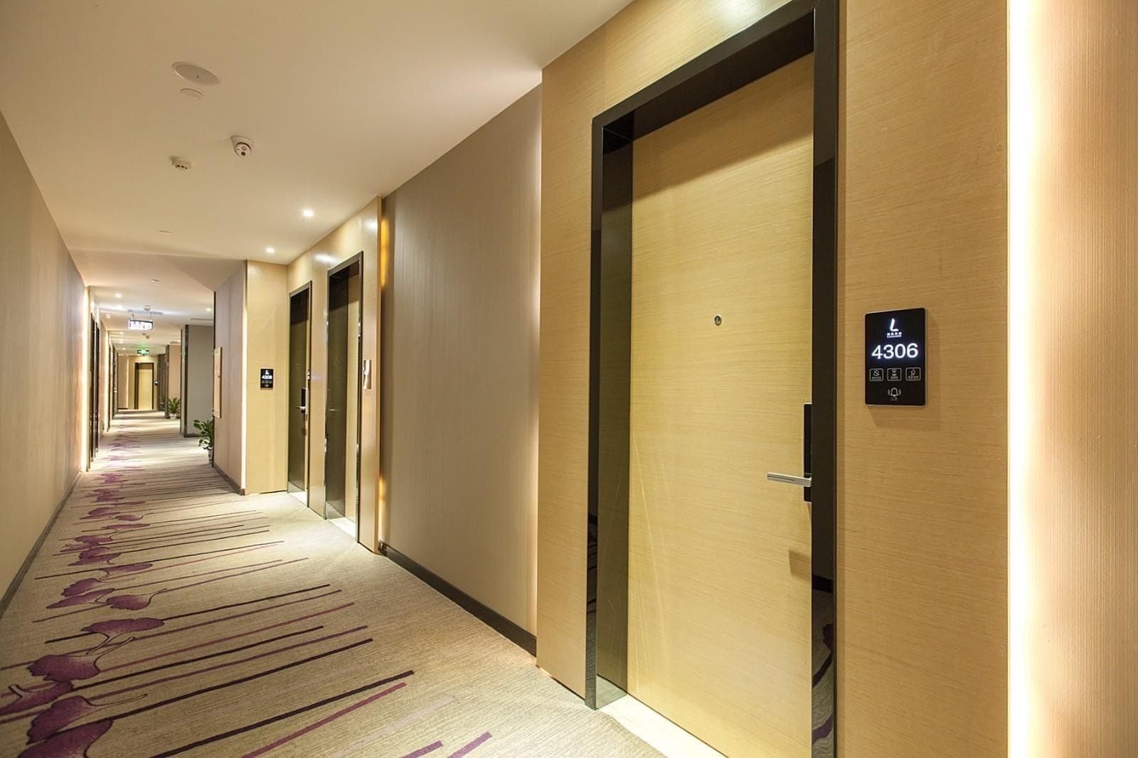 A hotel corridor with doors, a carpet with a purple pattern, and a sign indicating room number 4306.