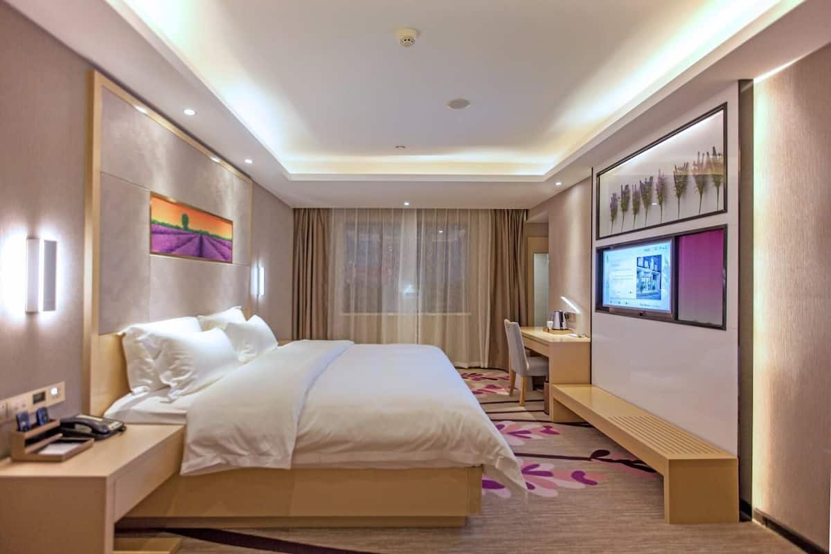 Una habitación de hotel con cama, mesita de noche, escritorio y un ventanal con cortinas.
