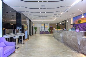 A hotel reception area with a marble floor, a reception desk, purple seating, and a large window with a sunset view. - Lavande Hotel (Wuhan)