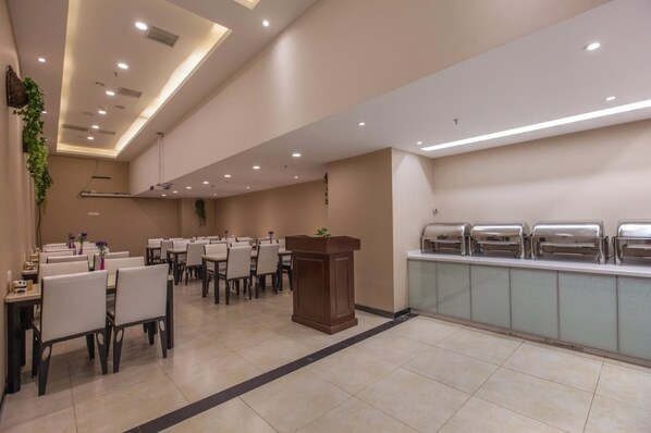 A conference room with multiple tables and chairs, a podium, and a buffet area with food dispensers. - Lavande Hotel (Wuhan)