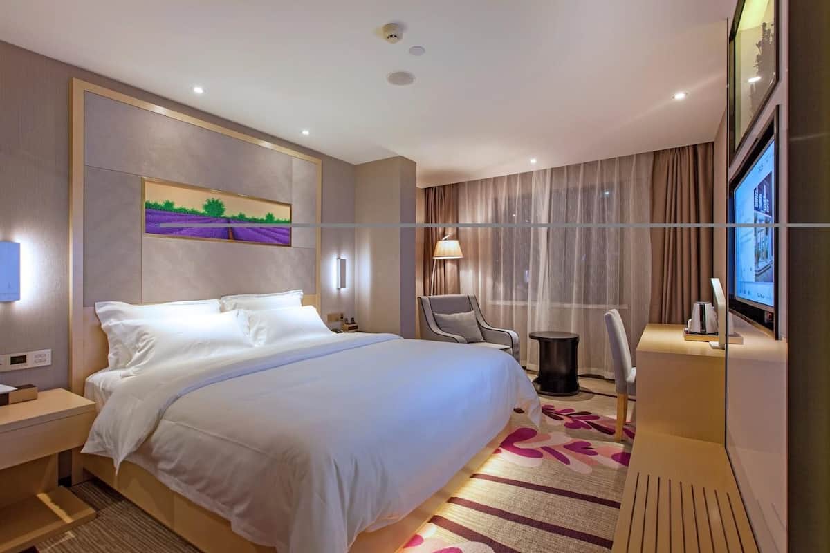 Habitación de hotel moderna con una cama grande, un escritorio, una silla, un televisor y un cuadro en la pared.