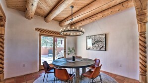 A dining area with a round table, six chairs, a chandelier, and a framed artwork on the wall.
