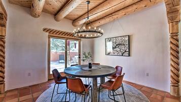 A dining area with a round table, six chairs, a chandelier, and a framed artwork on the wall.