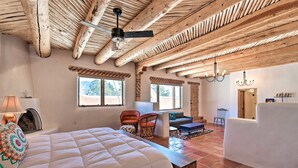A spacious room with a large bed, a wooden ceiling, and a view of the outdoors through windows.