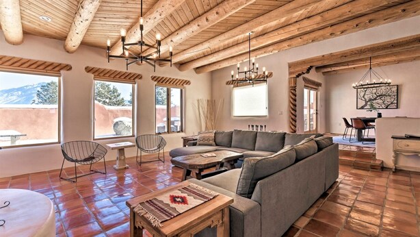 A spacious living area with a wooden ceiling, a gray sectional sofa, a round wooden table, and a dining area with a table and chairs.