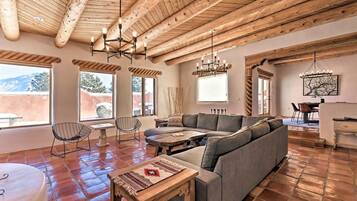 A spacious living area with a wooden ceiling, a gray sectional sofa, a round wooden table, and a dining area with a table and chairs.