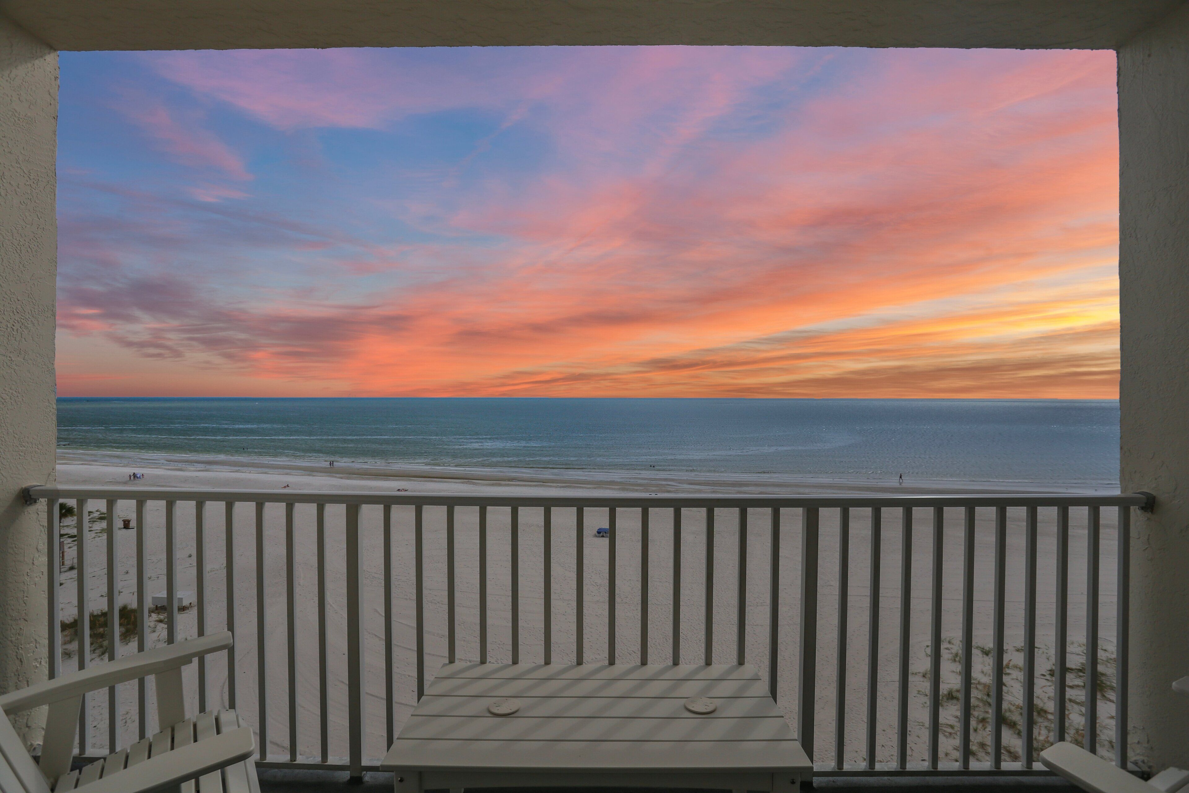 A balcony with a view of the beach and ocean during sunset.