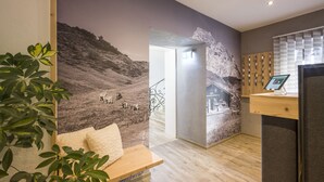 A modern hotel lobby with a mountain mural, a reception desk, and a wooden bench. - Haus Lukas (Hopfgarten im Brixental)
