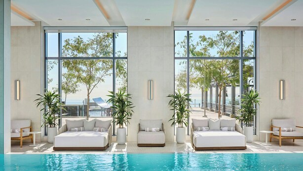A modern indoor pool area with large windows, white sofas, and potted plants. - The Pearle Hotel & Spa, Autograph Collection (Burlington)