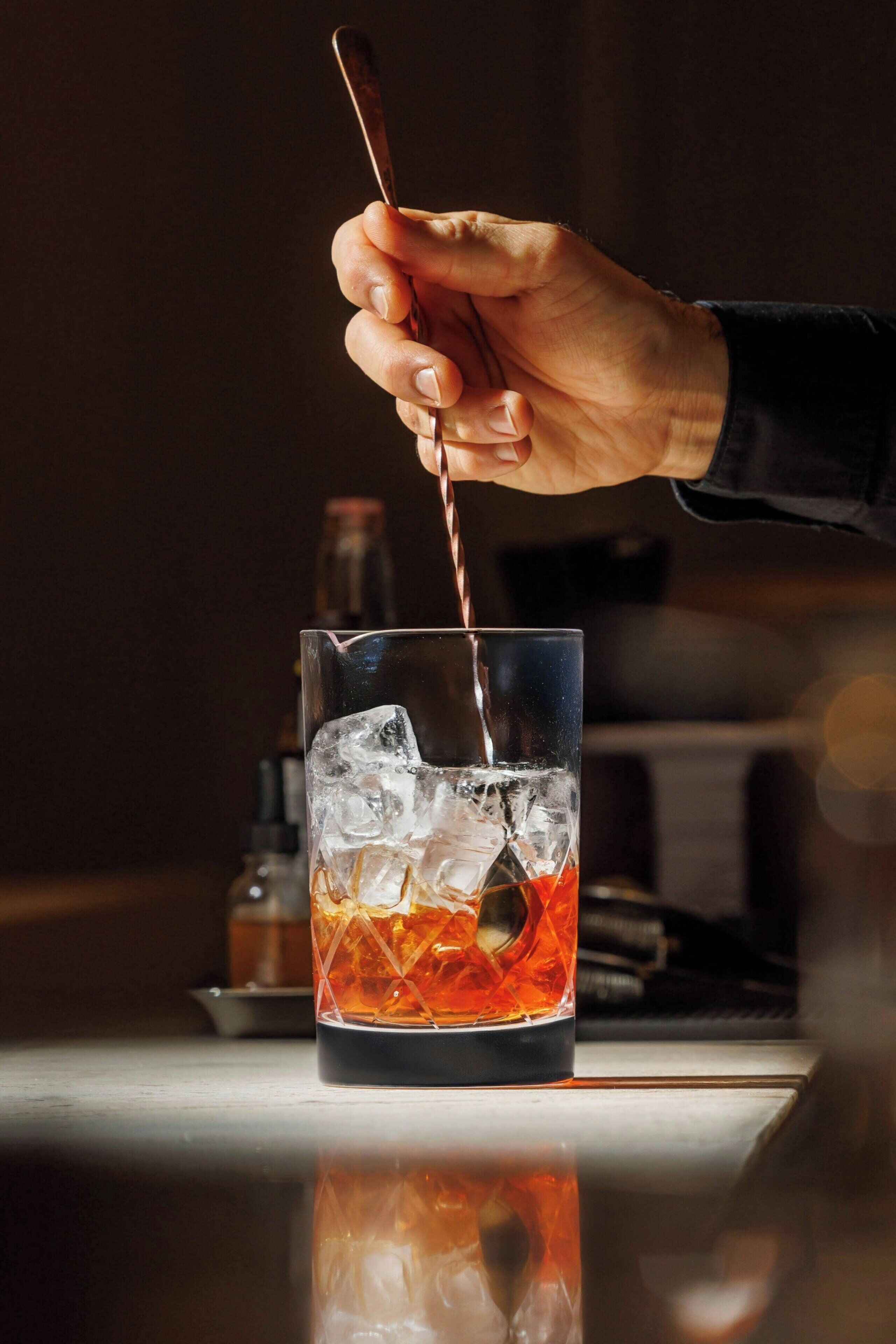 A hand pouring a drink into a glass with ice cubes.