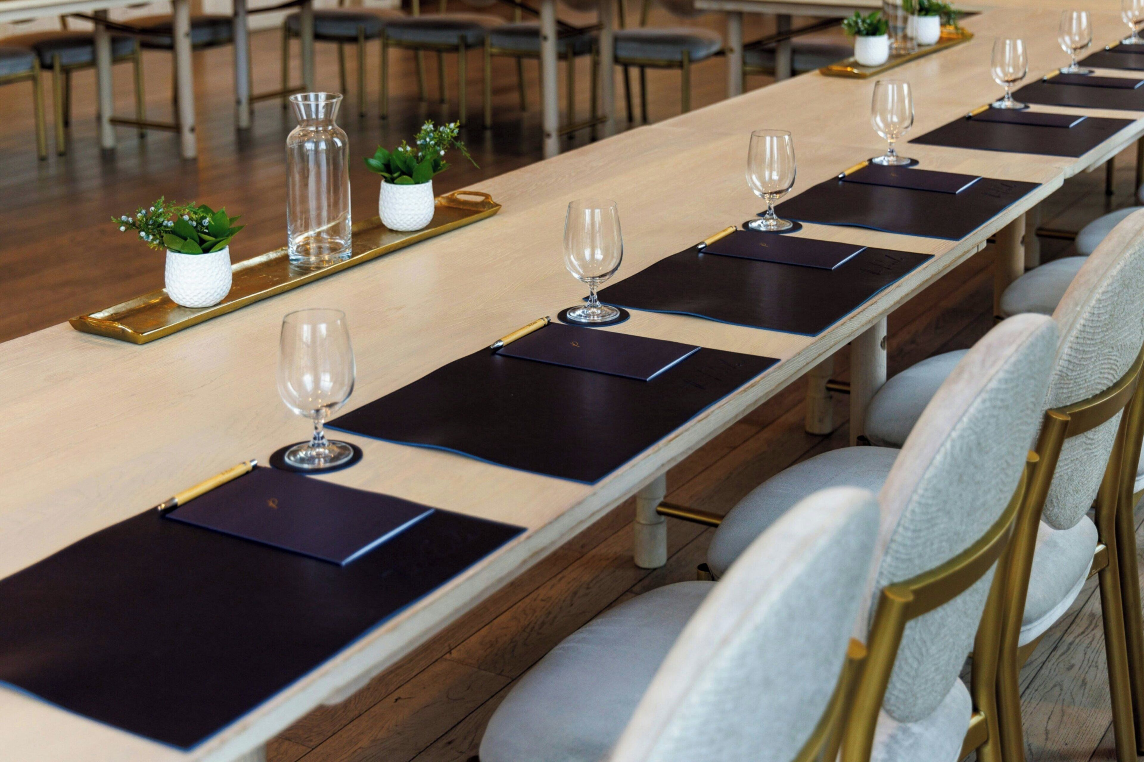 A long conference table with black placemats, clear glass vases, and small potted plants.