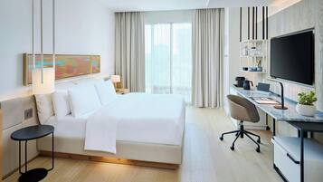 A modern hotel room with a large bed, a desk with a chair, a TV, and a window with curtains.