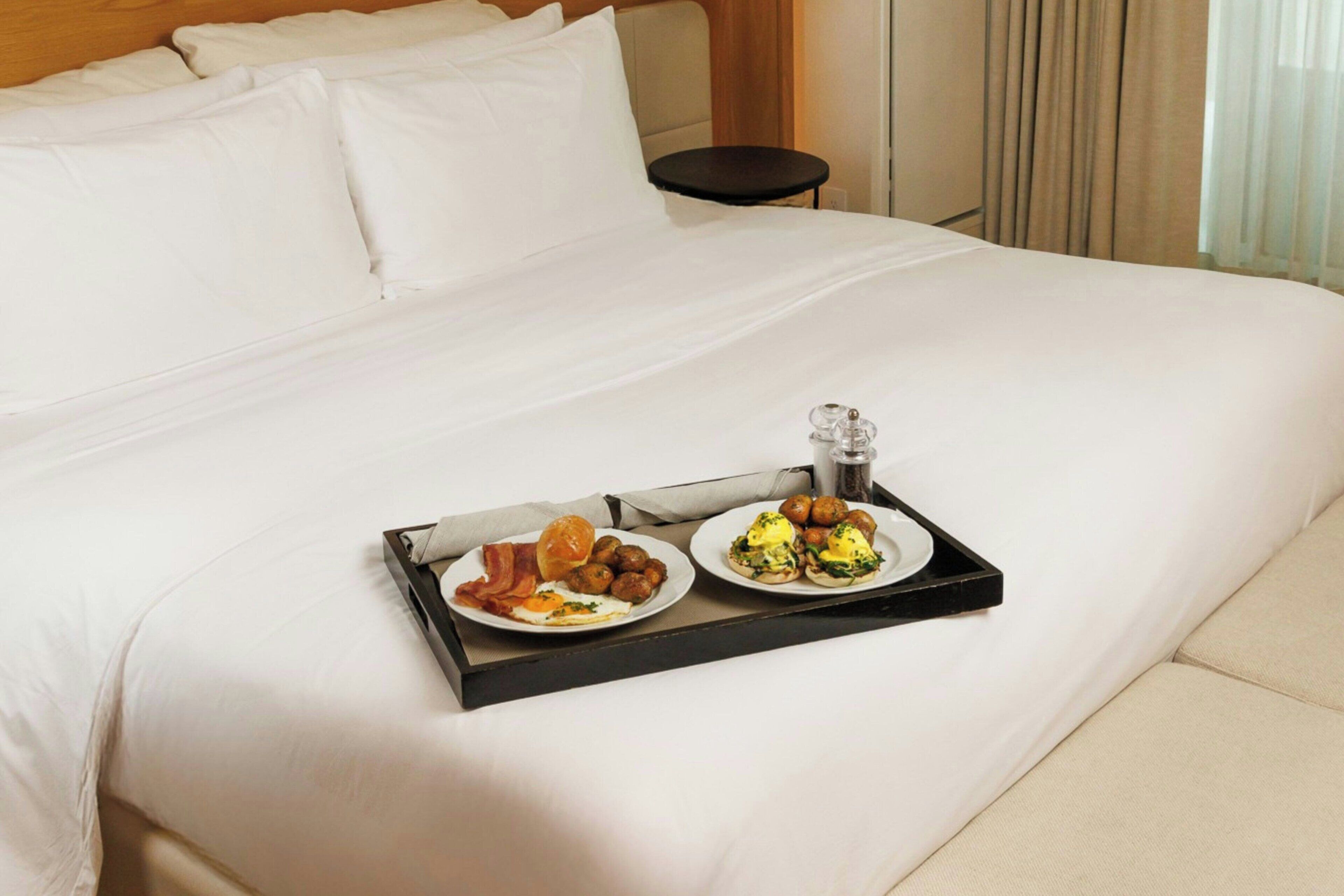 Una cama bien tendida con una bandeja de desayuno, que incluye huevos y salchichas, en una habitación de hotel.