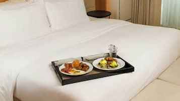 Una cama bien tendida con una bandeja de desayuno, que incluye huevos y salchichas, en una habitación de hotel.