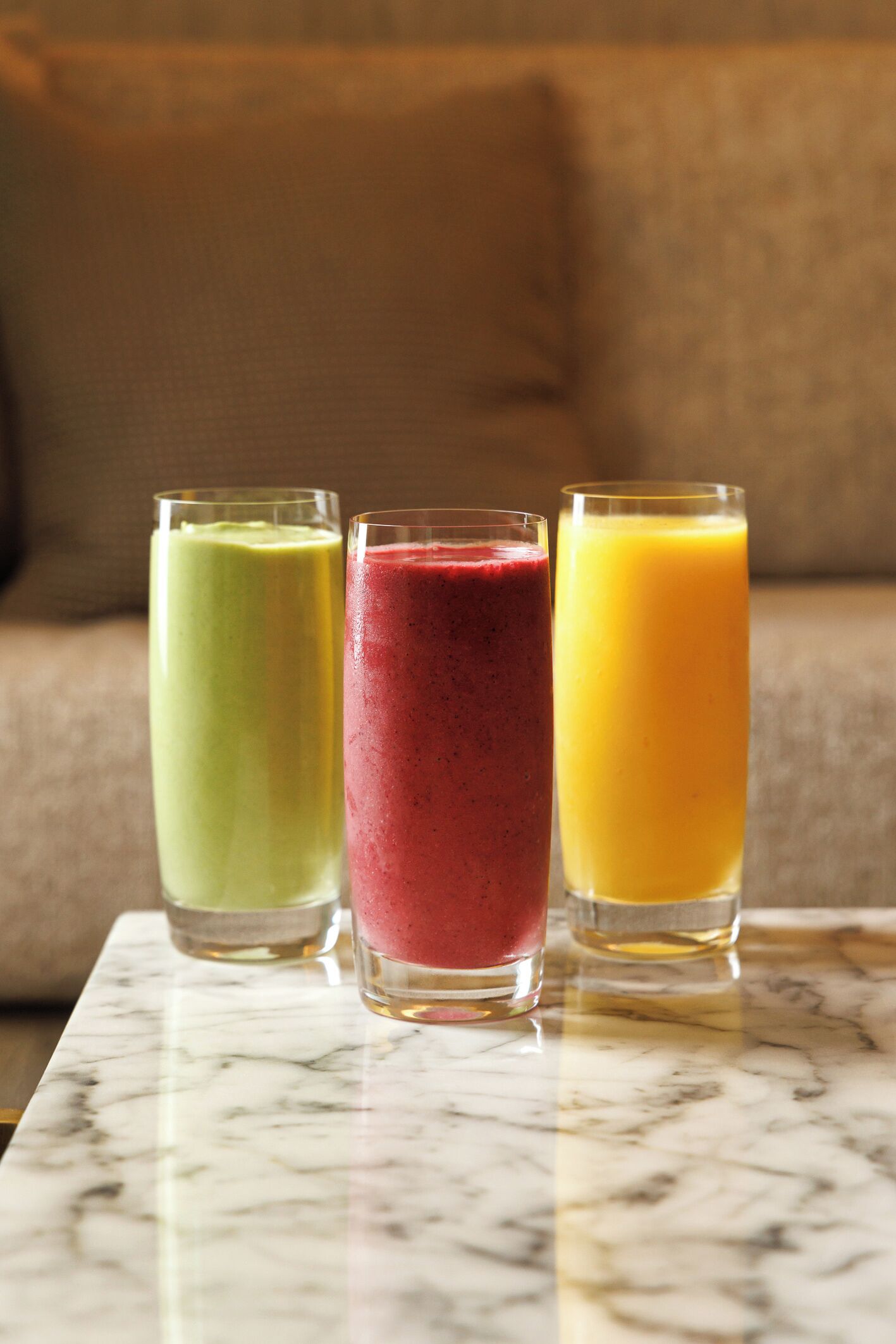 Three glasses of smoothies on a marble surface.