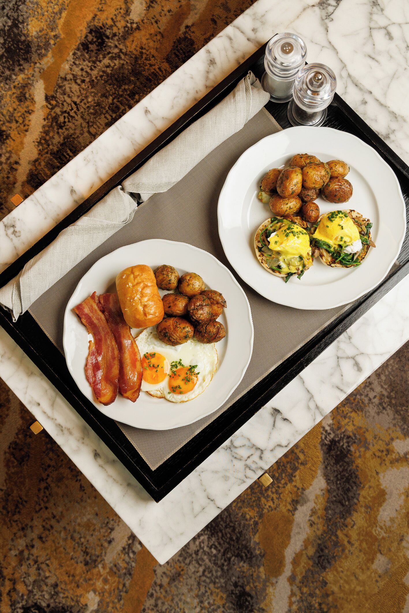 A tray with breakfast items including eggs, bacon, and sausages on a marble countertop.