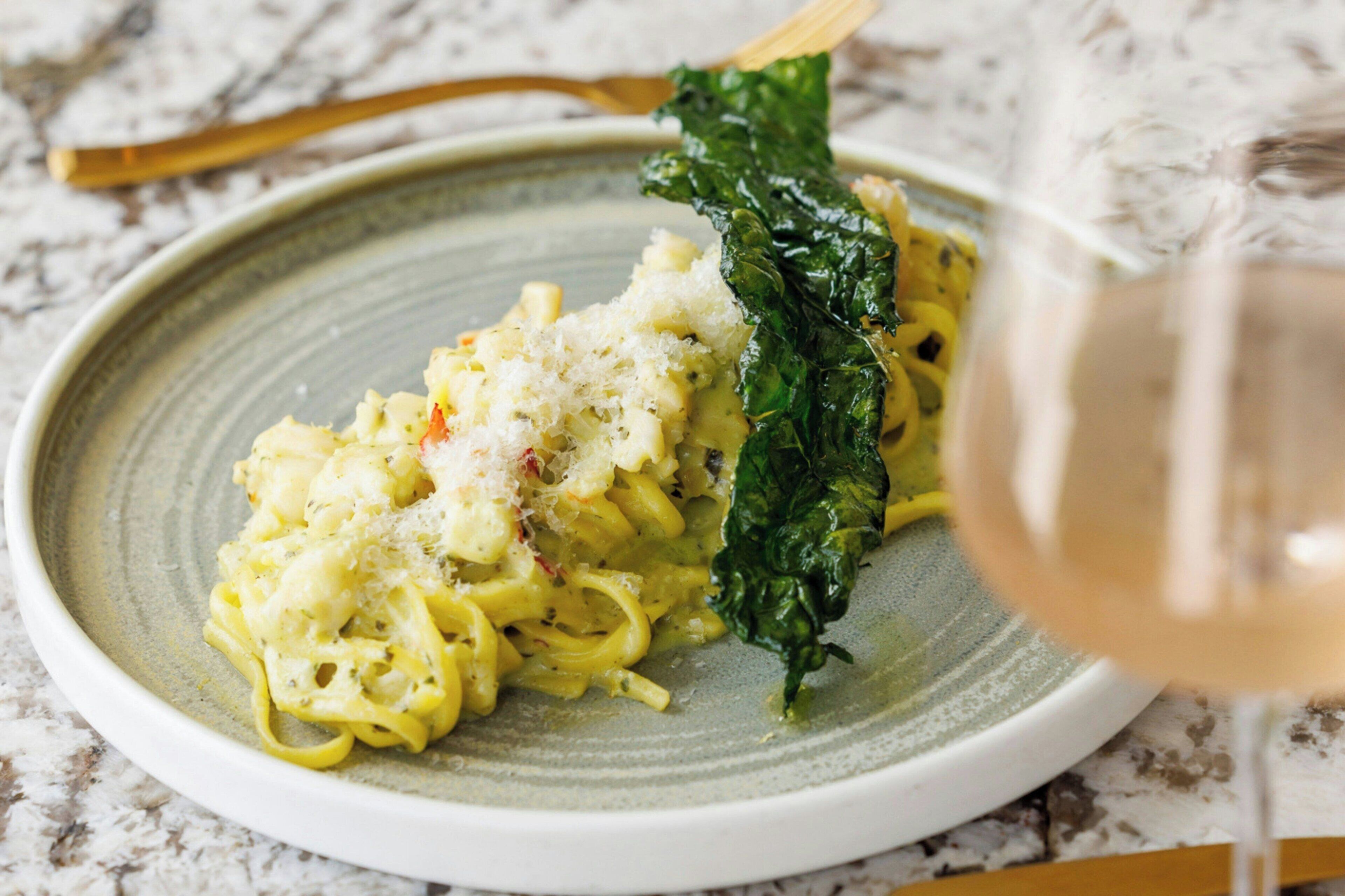 A plate of pasta with a side of greens and a glass of white wine.