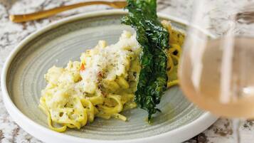 A plate of pasta with a side of greens and a glass of white wine.