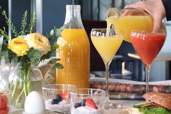 Una escena de desayuno con una botella de jugo de naranja, una copa de martini con una bebida roja y un sándwich sobre una mesa.