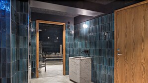 Un baño moderno con un lavamanos de mármol, azulejos azul oscuro y una puerta de madera.