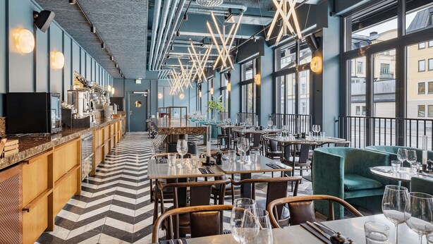 Un restaurante moderno con una barra larga, varias mesas y un suelo estampado.