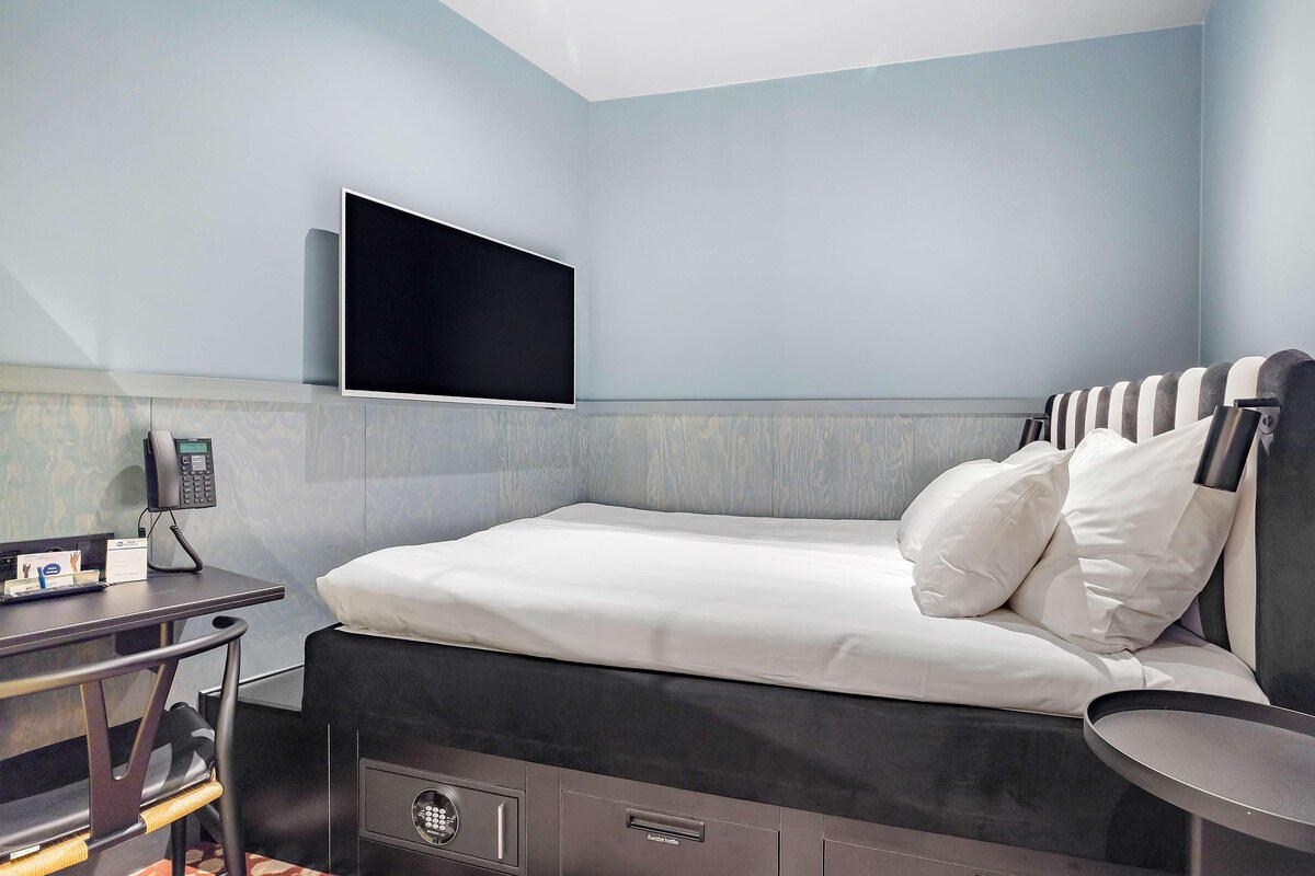 Una habitación de hotel moderna con una cama, un escritorio con teléfono y un televisor de pantalla plana montado en la pared.