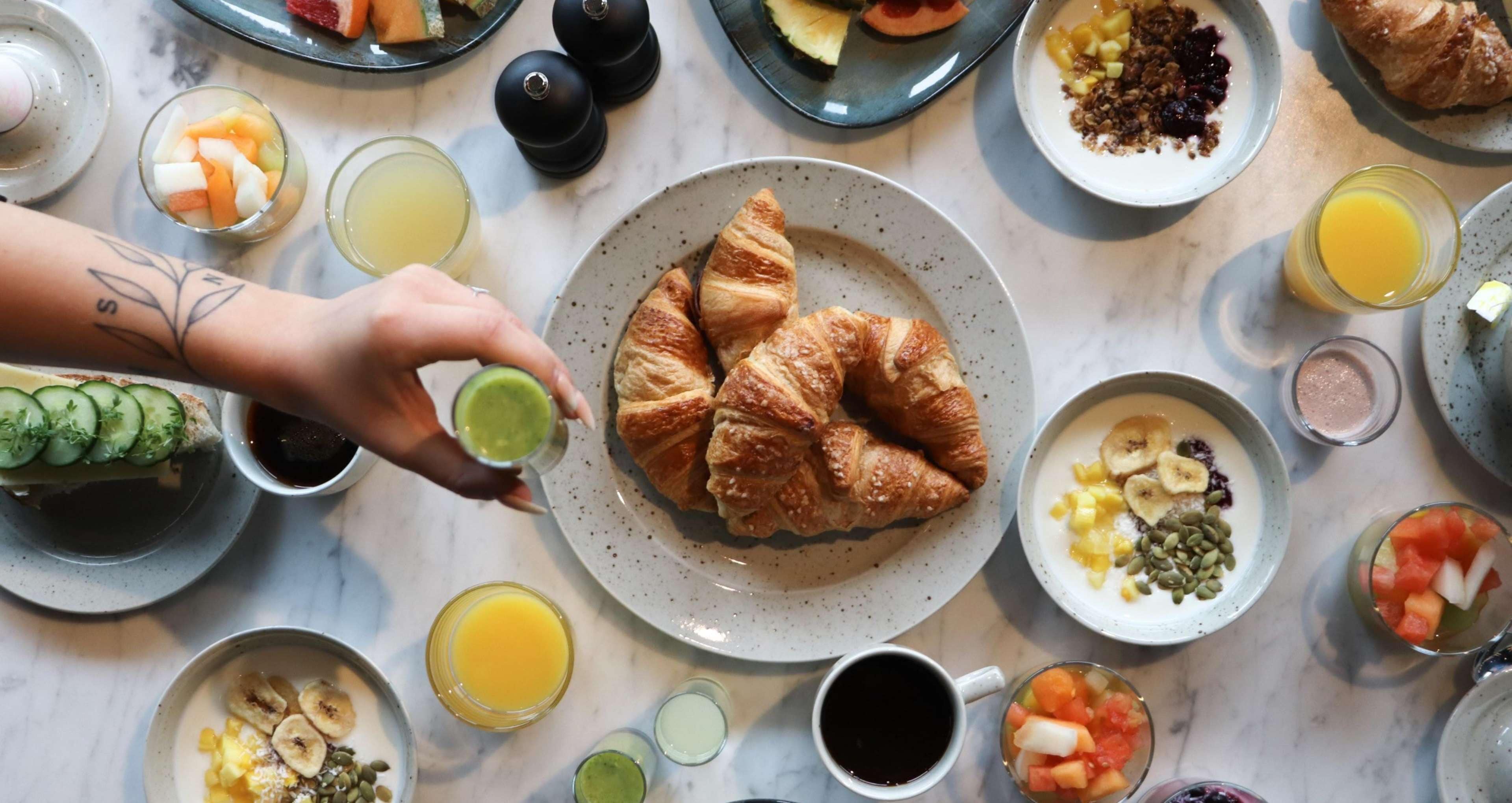 A breakfast table with croissants, fruit, and various beverages.
