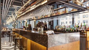 Zona de bar con mostrador de mármol, varios taburetes y una variedad de botellas y copas.