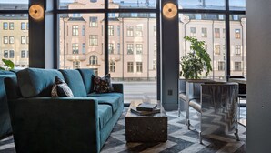 Un interior moderno con un sofá color turquesa, una mesa de centro de mármol y vistas a edificios a través de amplios ventanales.