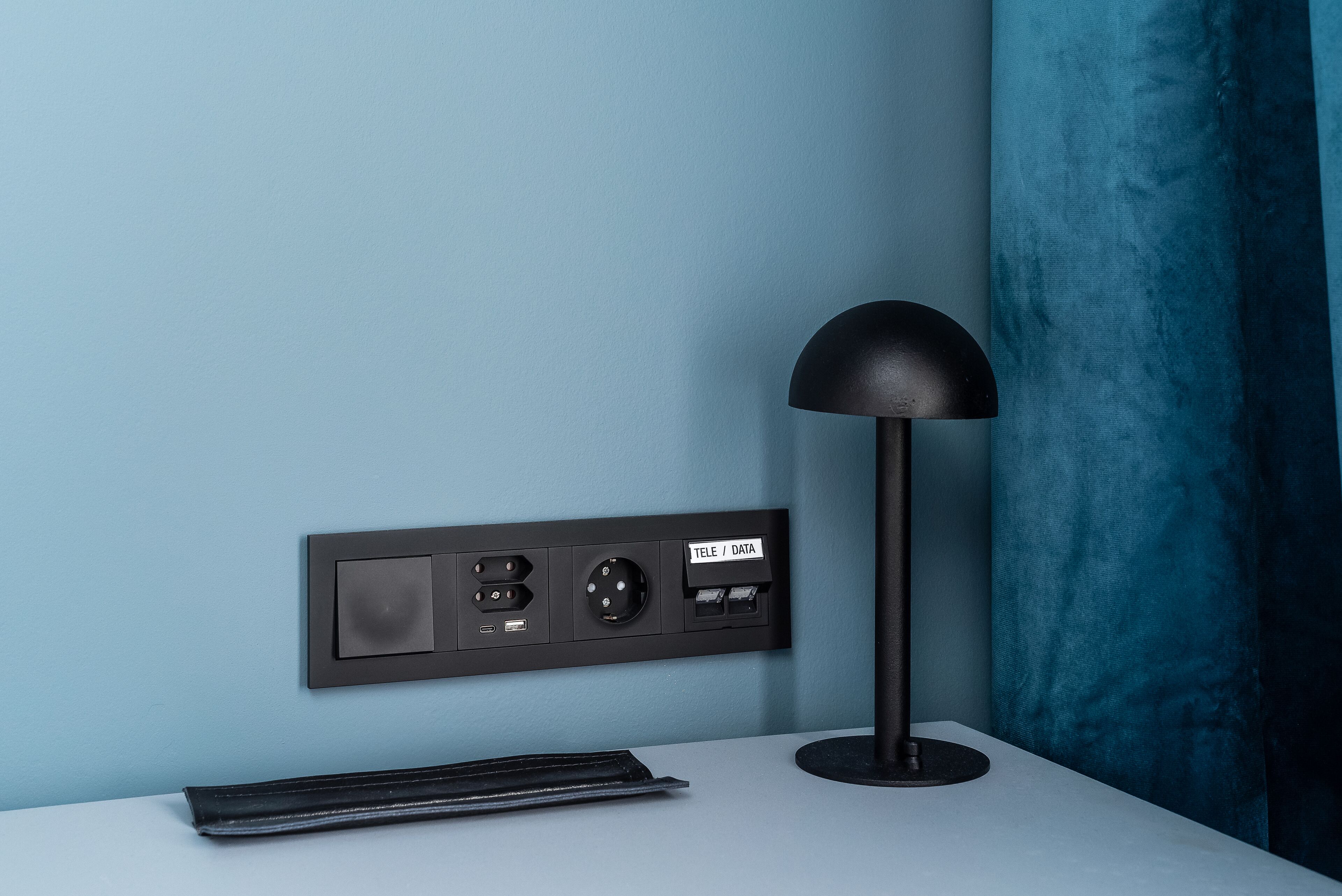 A desk with a lamp, a power strip with multiple sockets, and a label indicating 'TELE / DATA' connectivity.