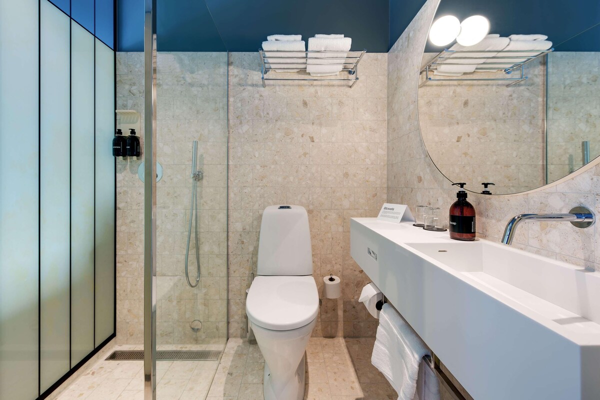 Un baño moderno con ducha de vidrio, inodoro blanco, espejo grande y lavamanos blanco con artículos de tocador.
