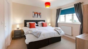A bedroom with a bed, bedside tables, a nightstand, a window with curtains, and a ceiling light fixture. - Apartment 4 (Worksop)